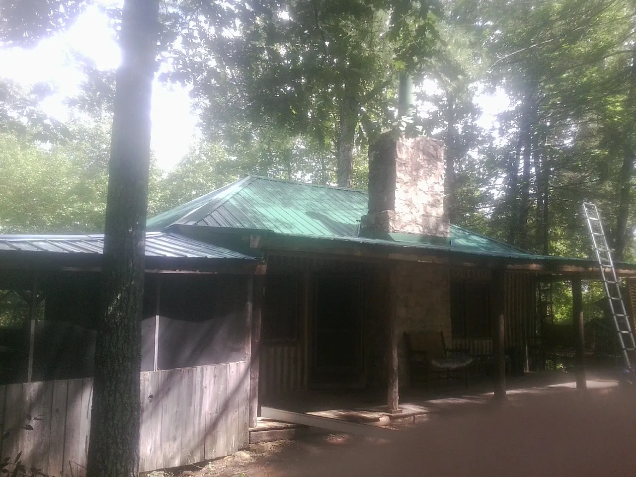 Green metal roof and stone chimney above a log cabin porch in Graysville